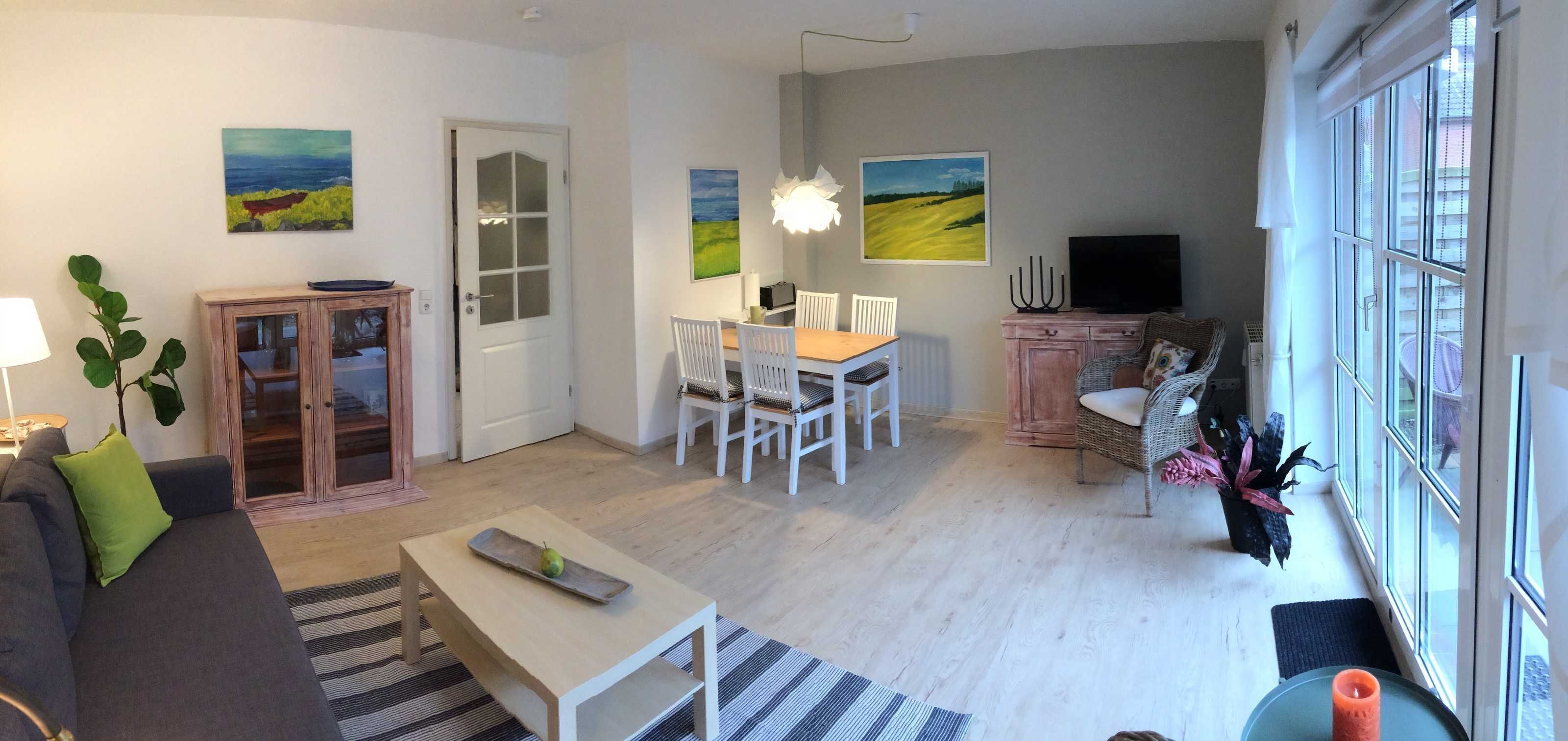 A living room with a sofa, a dining table with chairs, a television, and artwork on the walls.