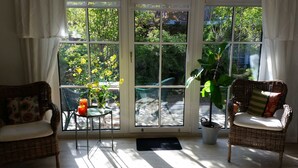 A sunlit room with wicker chairs, a small table with a vase and candles, and a view of greenery through large windows. - Wolke 7 Vacation Rental - - Wolke 7 Vacation Rental (Brodersby)