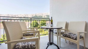Ein Balkon mit Korbmöbeln, einem kleinen runden Tisch und einer Weinflasche.