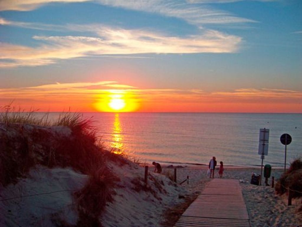 A sunset over the ocean with a boardwalk leading to the beach.