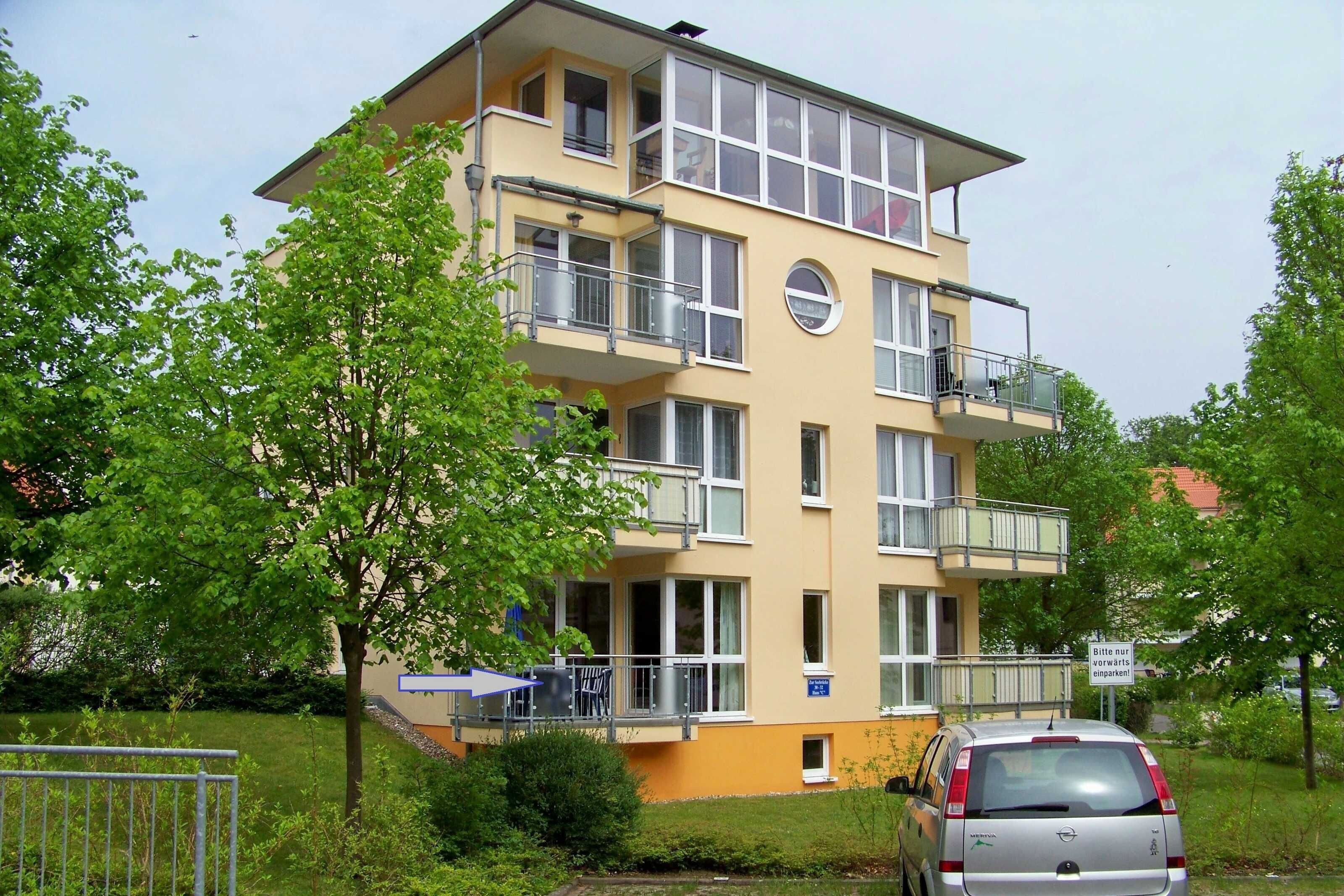 Un immeuble résidentiel à plusieurs étages, doté de balcons, avec une voiture garée devant et une enseigne en allemand.
