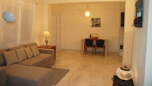 A living room with a sofa, a table with chairs, a lamp, and a painting on the wall. - Elounda Theo Villa (Agios Nikolaos)