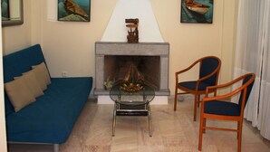 A living room with a fireplace, a blue sofa, two wooden chairs, and two paintings on the wall. - Elounda Theo Villa (Agios Nikolaos)