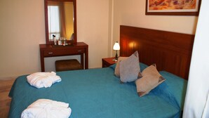A hotel room with a bed, a desk with a mirror, a lamp, and a painting on the wall. - Elounda Theo Villa (Agios Nikolaos)