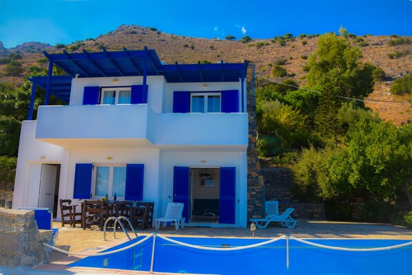 A two-story building with a pool area, outdoor seating, and a mountainous backdrop.