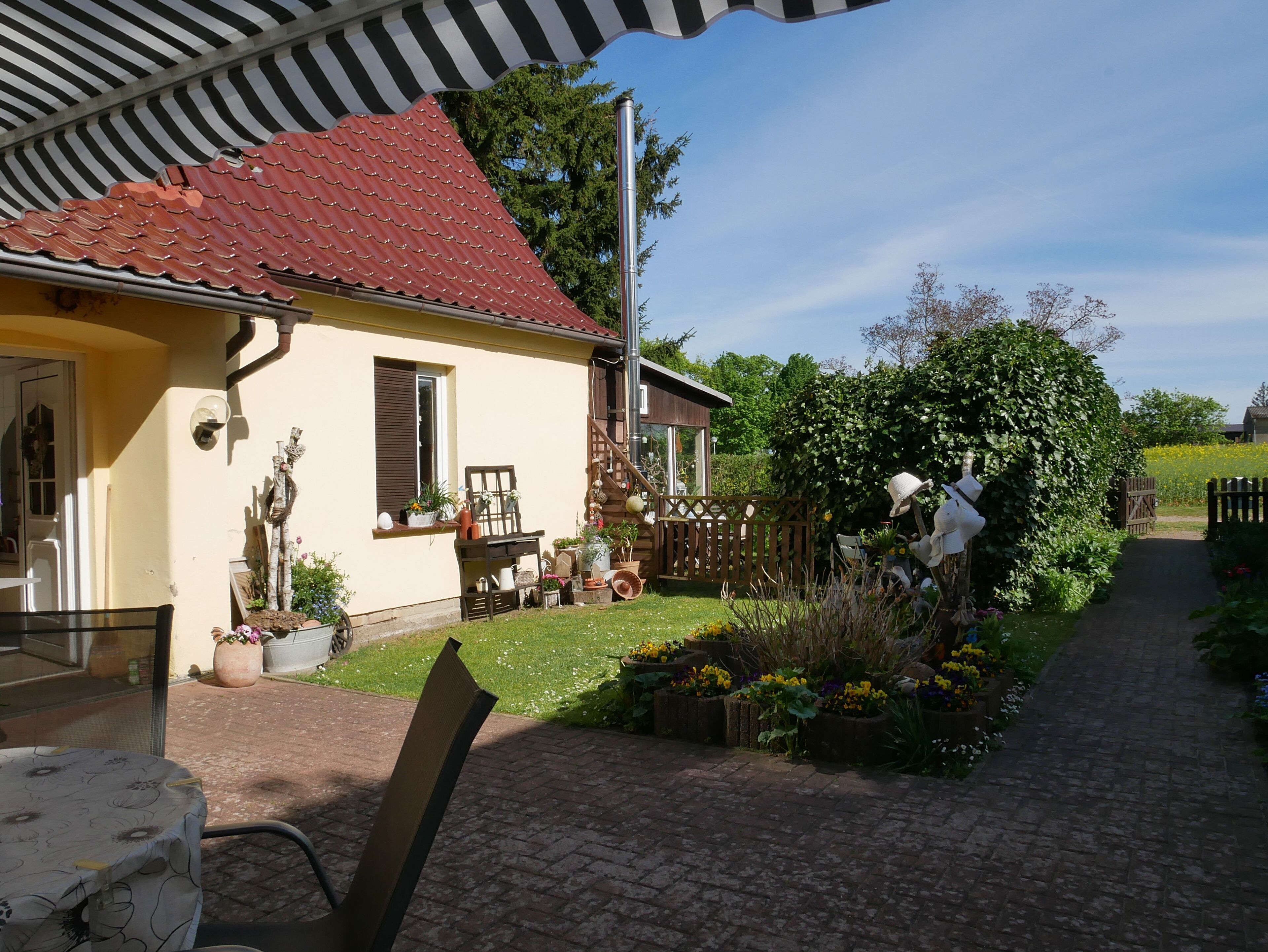 A house with a red tiled roof, a garden with various plants and flowers, a wooden fence, and a paved pathway.