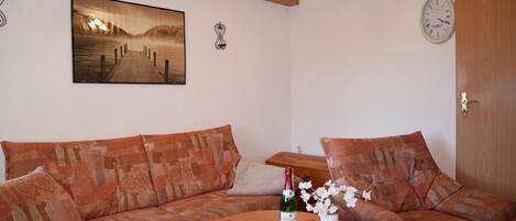 A cozy living room with a sofa, a wooden coffee table, a painting, a clock, and a door.