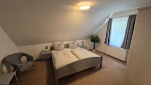 A bedroom with a bed, bedside tables, a chair, a plant, and a window with curtains.