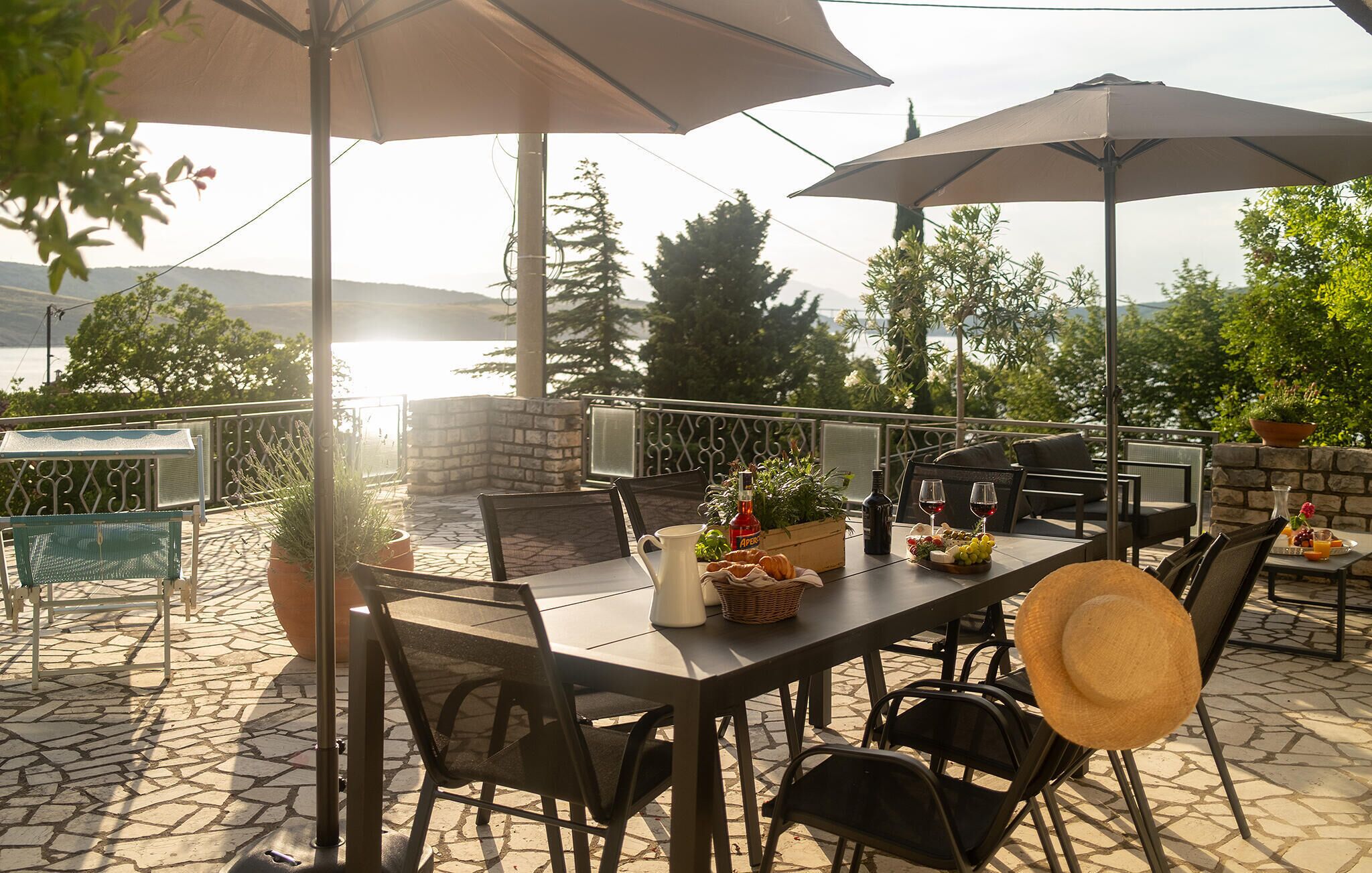Een terras buiten met een eettafel, omringd door stoelen en parasols, met uitzicht op een prachtig landschap.