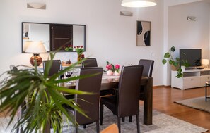 Un espace de salle à manger moderne, avec une table dressée pour quatre personnes, entourée de chaises, d’un téléviseur et d’objets décoratifs.