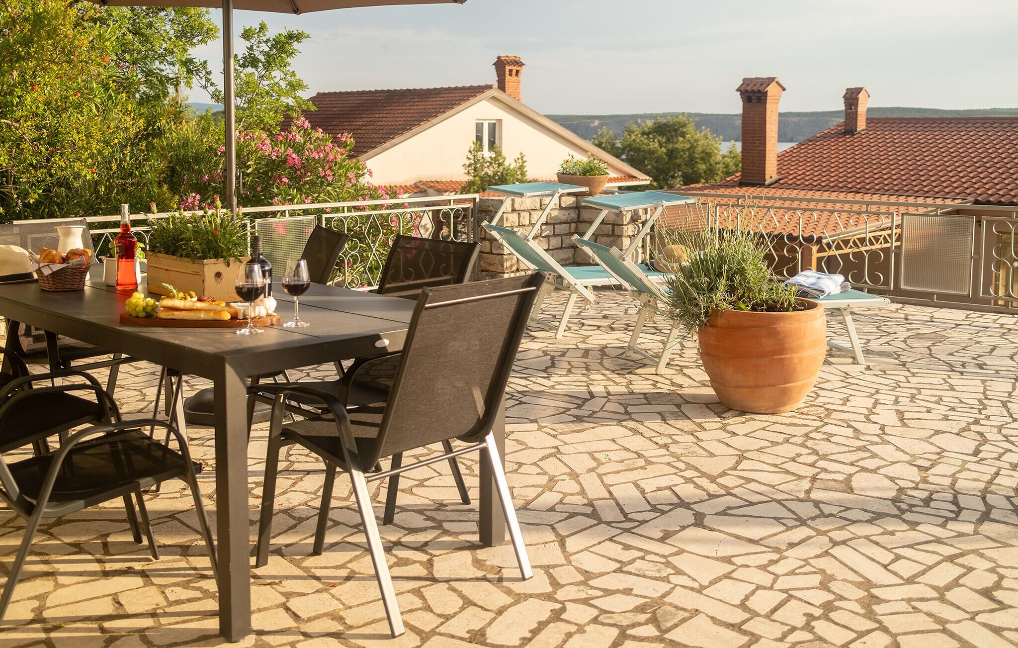 Un patio al aire libre con una mesa lista para comer, sillas, una planta en maceta y vistas de un edificio con techo de tejas.