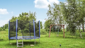 Un trampoline doté d’un filet de sécurité, installé dans un espace extérieur recouvert d’herbe.