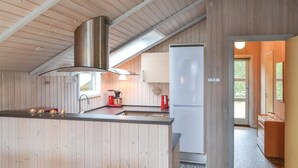 Een compacte keuken met houten wanden, een centraal eiland, een fornuis, een koelkast en een raam dat natuurlijk licht binnenlaat.