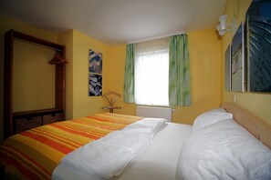 Une chambre d’hôtel avec un grand lit, une tête de lit en bois, une fenêtre avec des rideaux verts et un luminaire fixé au mur.