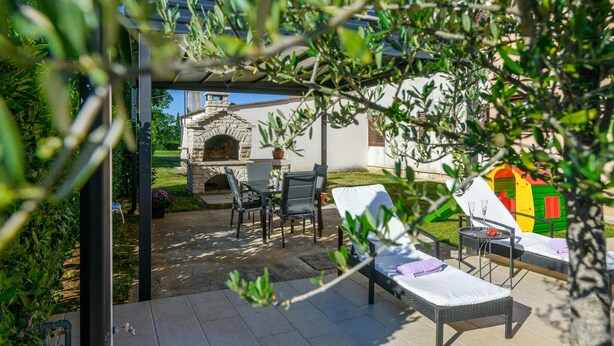 Eine Terrasse im Freien mit einem Kamin aus Stein, einem Esstisch und zwei Lounge-Stühlen.