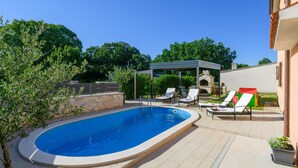 Ein Swimmingpool mit Liegestühlen und Grillplatz.