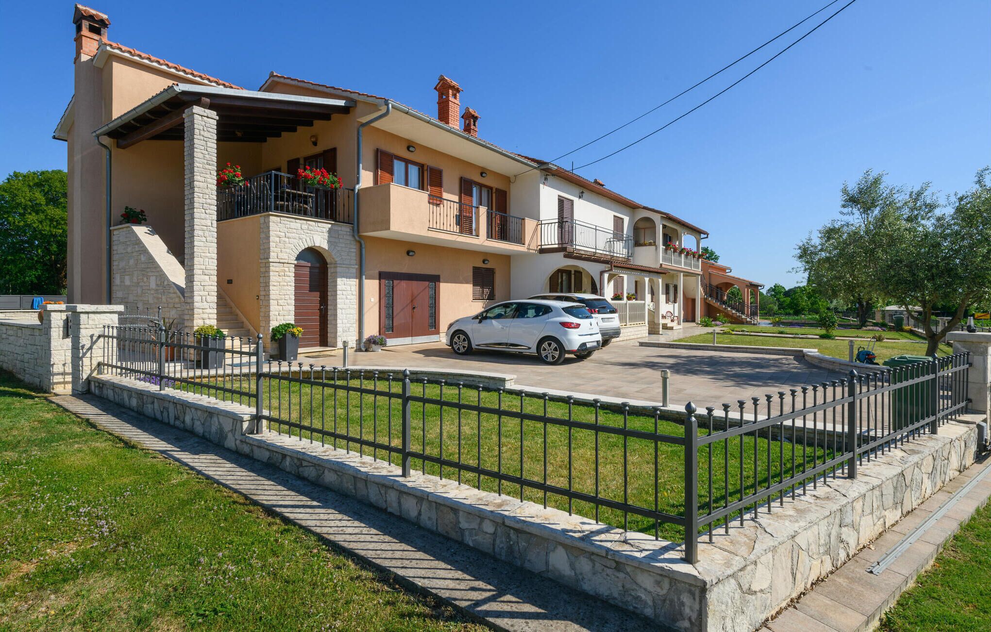 A two-story house with a stone facade, a balcony with plants, and a parked car in the driveway.