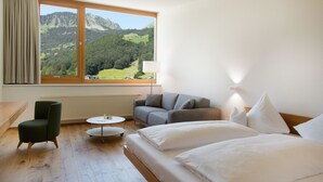 Una habitación de hotel con cama, sofá, sillón, una mesita y ventana con vista a la montaña.