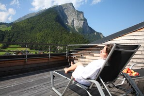 A person relaxing on a deck chair with a mountain view, a wooden deck, and a plate of apples.