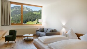 Una habitación de hotel con cama, sofá, sillón, una mesita y ventana con vista a la montaña.