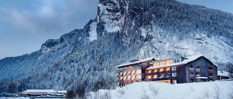 A mountain lodge with a river in front, surrounded by snow-covered trees.
