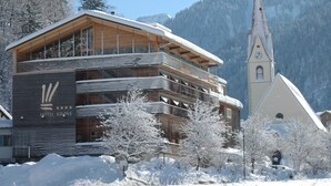 A hotel with a modern design, a prominent clock tower, and a snowy mountain backdrop.