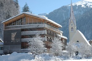 A hotel with a modern design, a prominent clock tower, and a snowy mountain backdrop.