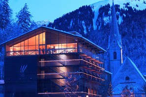 A modern building with a large glass facade, a visible staircase, and a church in the background.