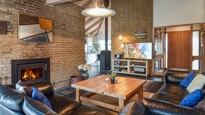 A cozy living room with a fireplace, leather sofa, wooden coffee table, and a TV.