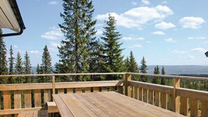 Une terrasse en bois avec une table et des bancs, d’où l’on peut admirer une forêt et des montagnes lointaines.