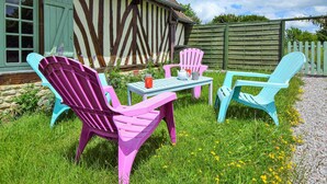 Un jardin avec une table et deux chaises, une maison à la façade distinctive, avec des éléments en bois apparent, et une clôture en bois en arrière-plan.