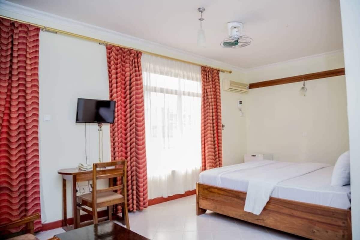 A bedroom with a bed, a desk, a chair, a television, and curtains.