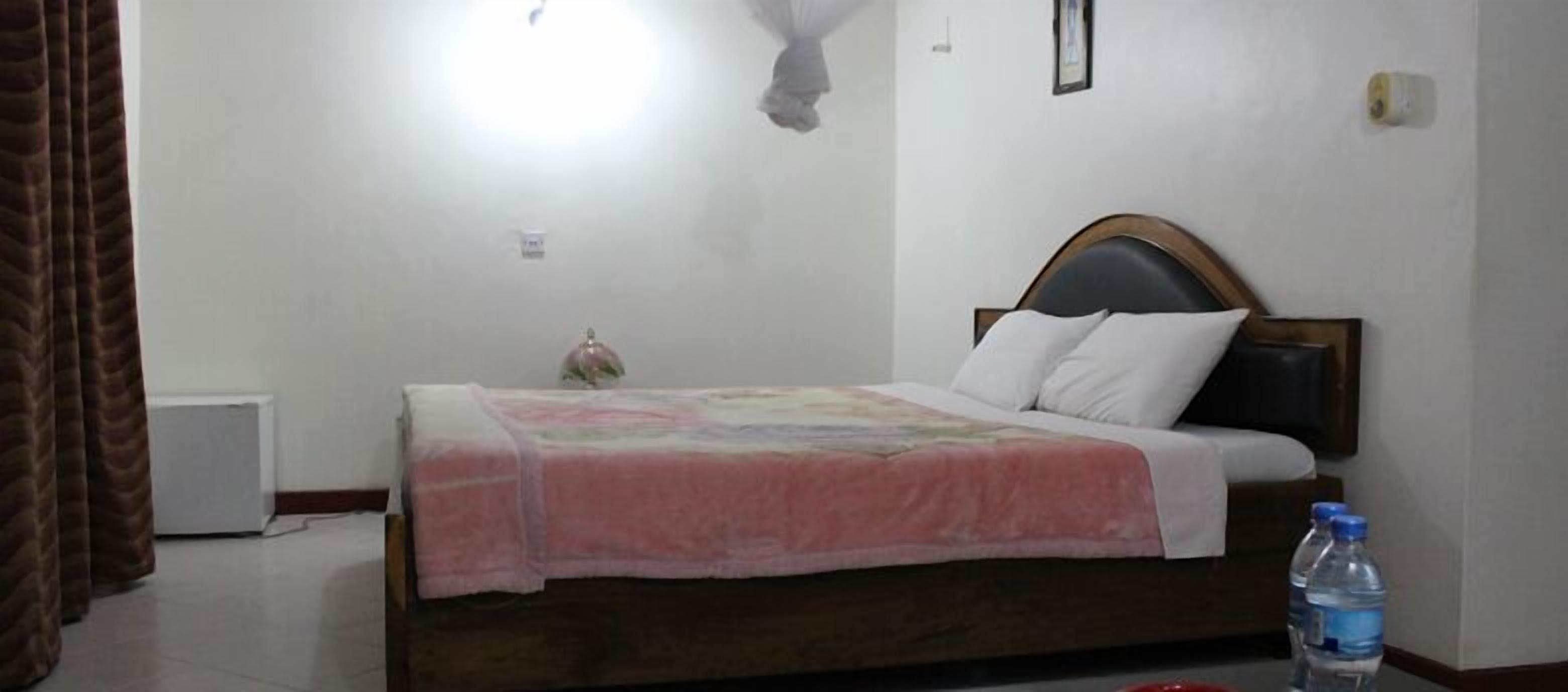 Un dormitorio con una cama, una mesita de noche, una botella de agua y una lámpara fijada a la pared.