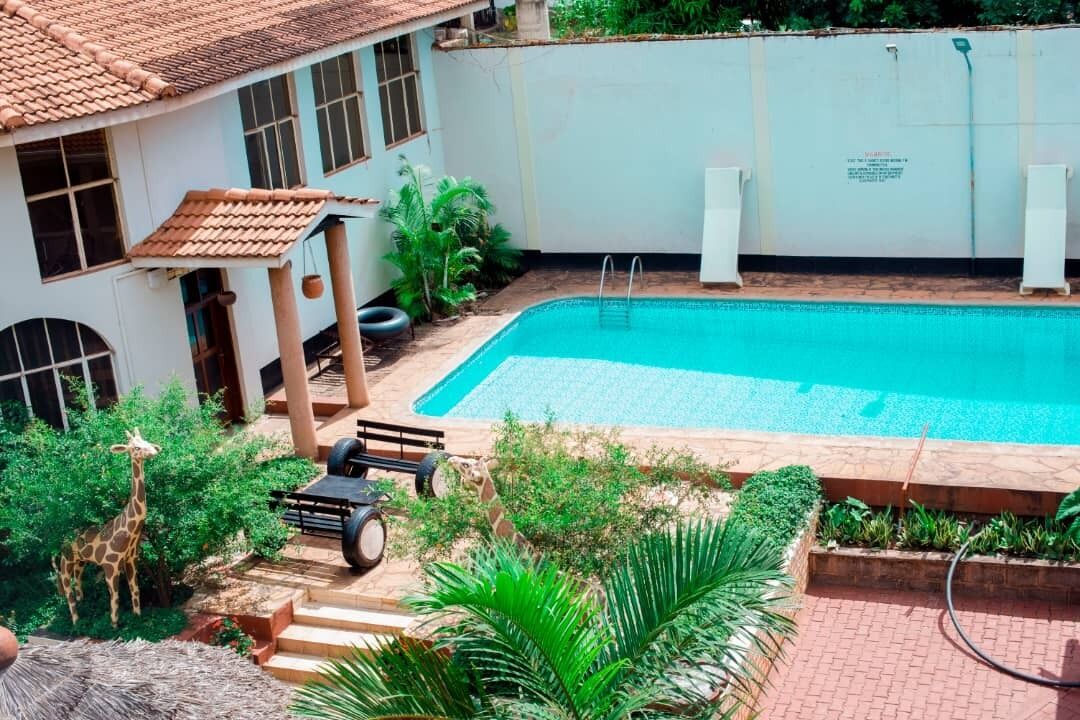 Piscina rodeada por vegetação, um pequeno gazebo e um edifício com telhado de azulejos.