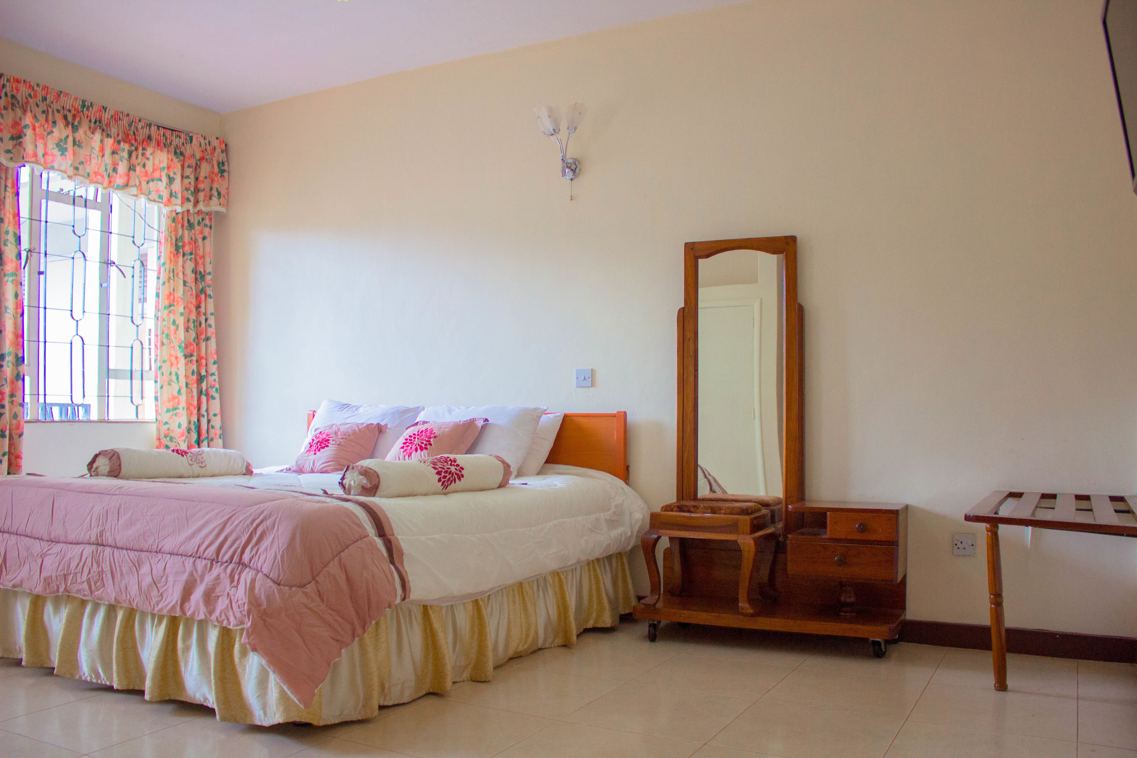 Un dormitorio con cama, cómoda, espejo y ventana con cortinas.
