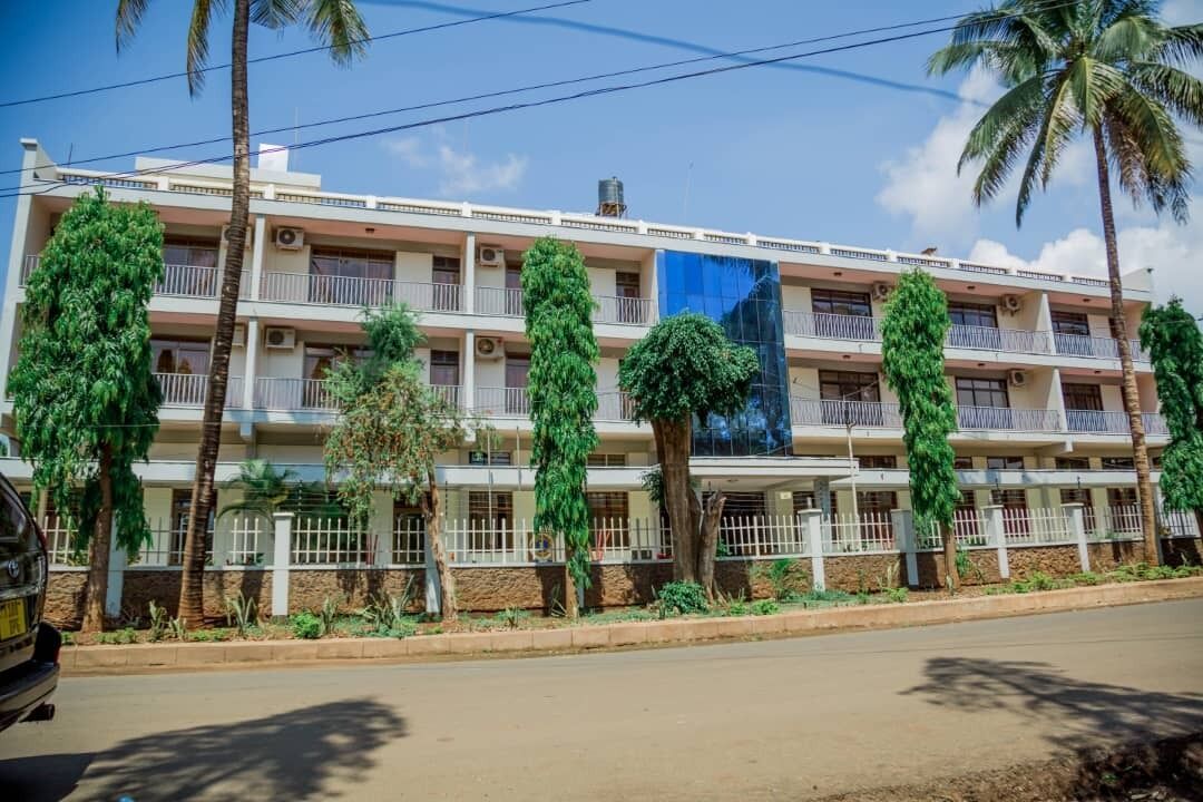 A multi-story building with balconies, surrounded by palm trees and greenery.