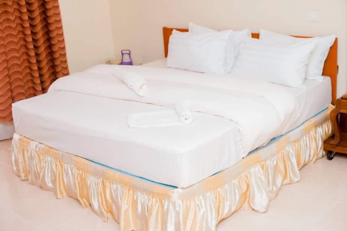 A neatly made bed with white linens and a gold-trimmed base, a wooden headboard, and a purple object on the nightstand.