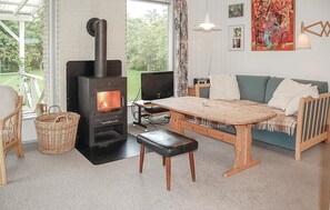 Relax in this inviting living room with a wood-burning stove, comfortable sofa, and large window offering a view of the surrounding greenery.