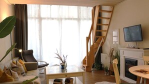 A living room with a sofa, coffee table, and a fireplace. There is a TV mounted on the wall and a staircase leading to an upper level.