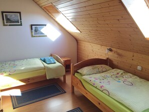 Quarto de estudante com duas camas de solteiro, teto de madeira e um claraboia.