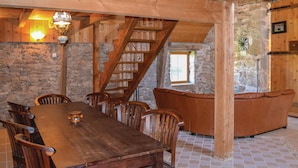 A rustic dining area with a wooden table and chairs, a stone wall, and a wooden staircase.