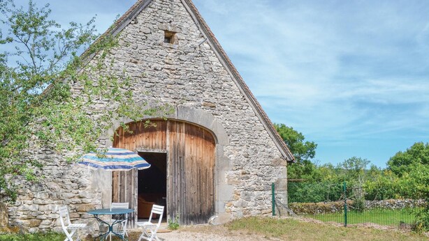 A stone building with a wooden door and a small window. There is a table with chairs and an umbrella outside.
