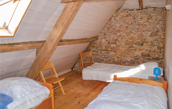 A small, rustic room with a sloped ceiling, wooden beams, a stone wall, two single beds, a wooden chair, and a small table with a lamp. - Awesome home in Padirac with WiFi (Padirac)