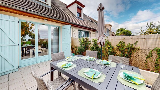 Een buiten eetgedeelte met een tafel voor vier personen, omringd door rieten stoelen, onder een pergola.