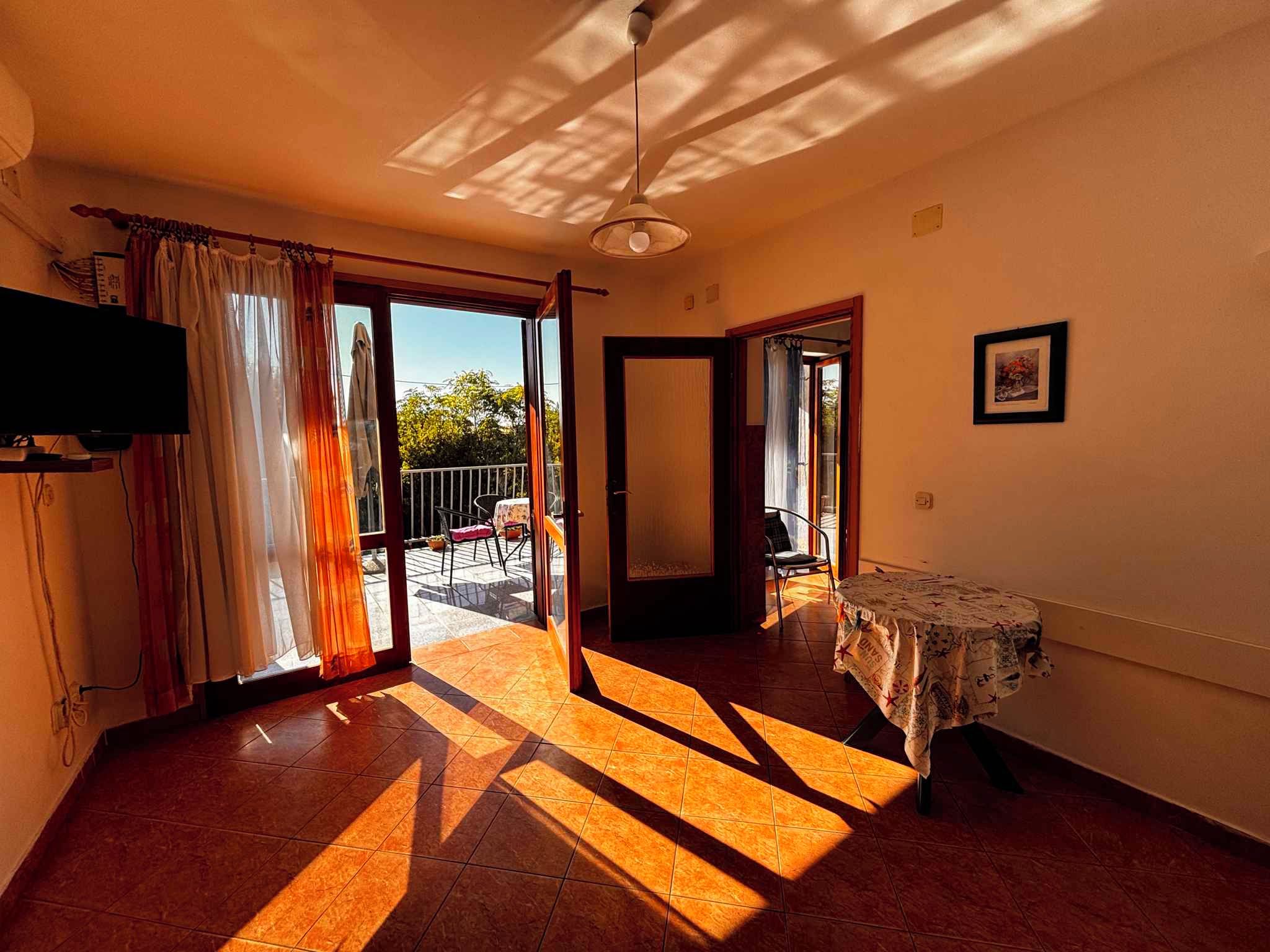 A room with a large sliding glass door leading to an outdoor area, a ceiling fan, and a table with a tablecloth.