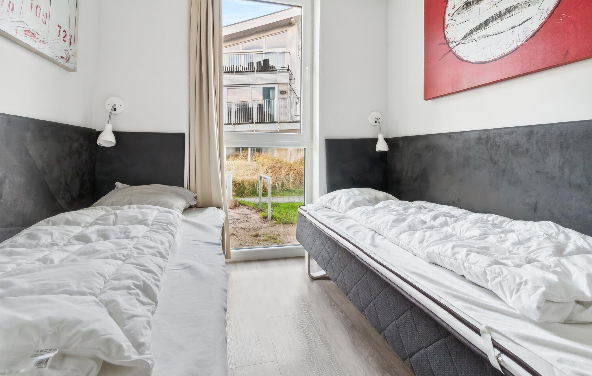 A bedroom with two beds, a window with a view of a building, and a red artwork on the wall.