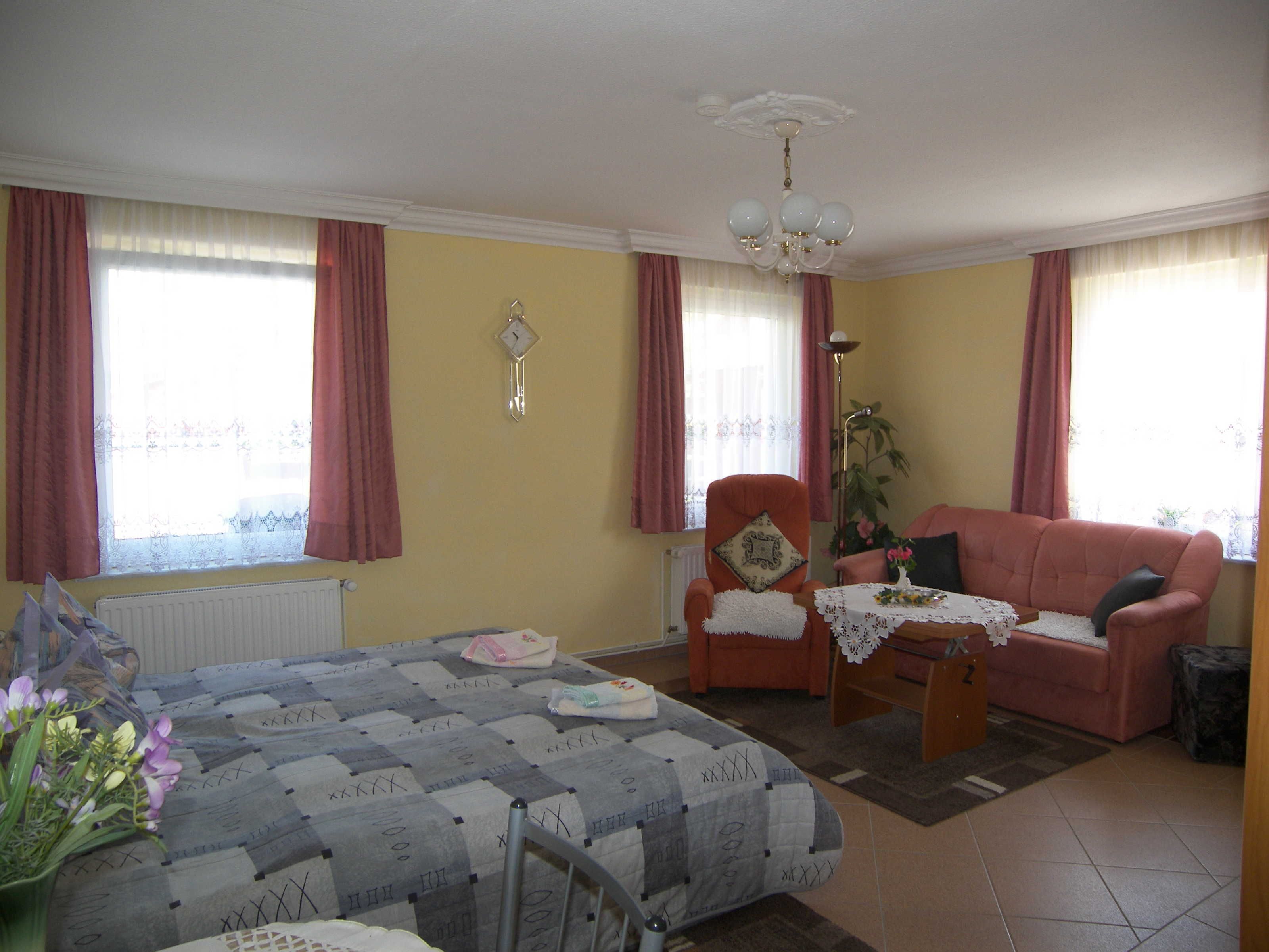 A living room with a sofa, armchair, and a bed with a quilt.