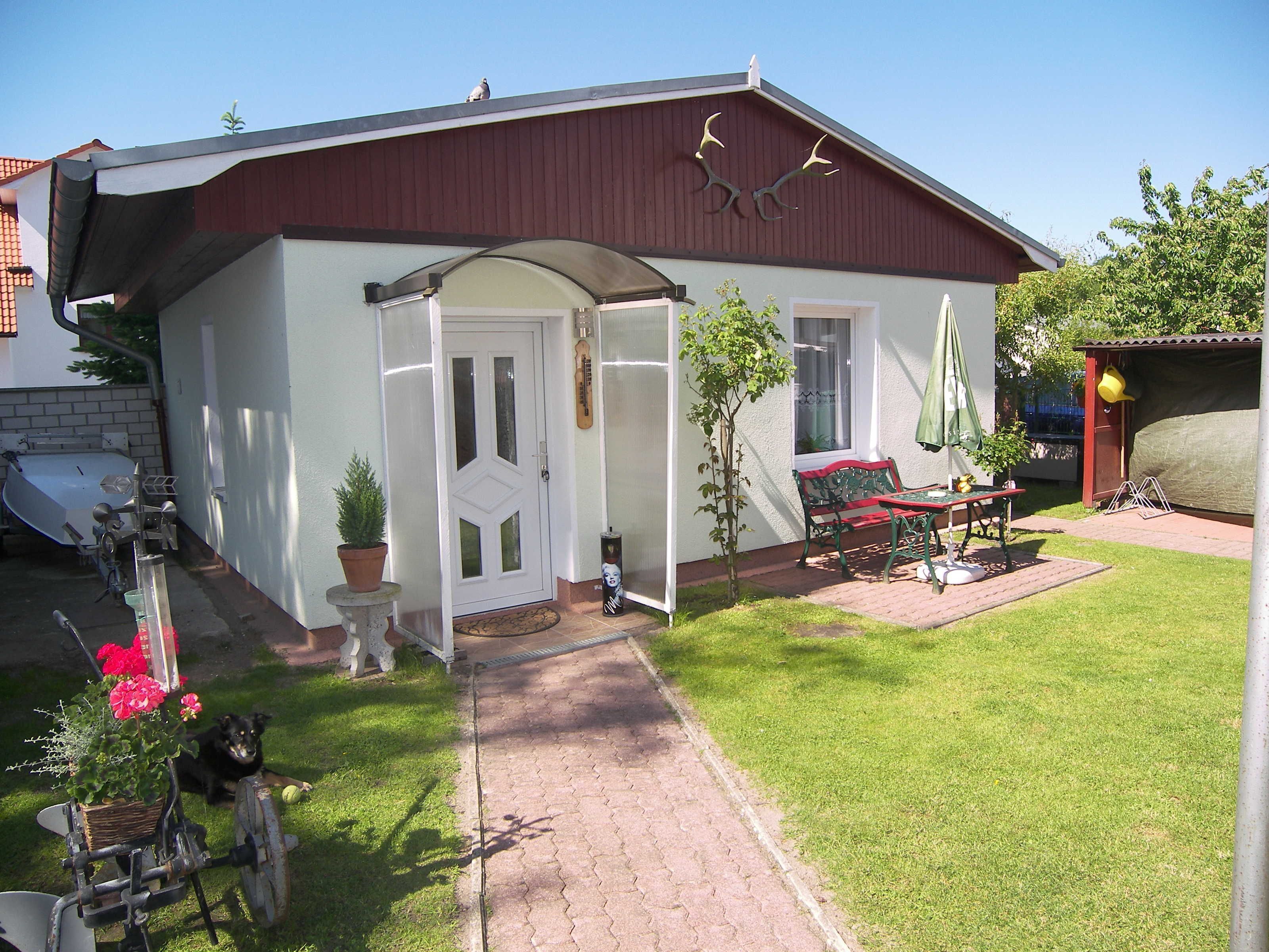 Una casa con fachada blanca, techo rojo y un pequeño jardín con un banco y una mesa.