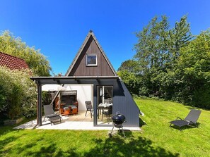 Una casa a forma triangolare con una veranda coperta, posti a sedere esterni e un barbecue.
