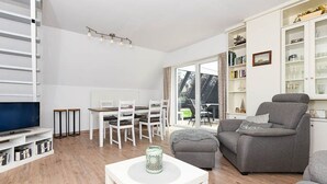 Un salon moderne avec un téléviseur à écran plat, des meubles blancs, un canapé gris et une bibliothèque.